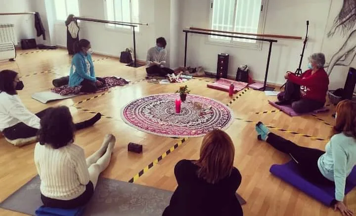 Participantes sentadas en el suelo alrededor de un mandala en una sala de yoga