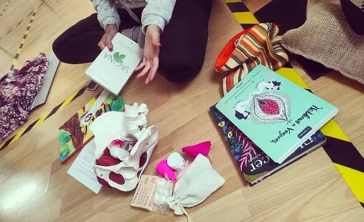 Libros, bolsas y material de un taller sobre salud femenina colocados en el suelo