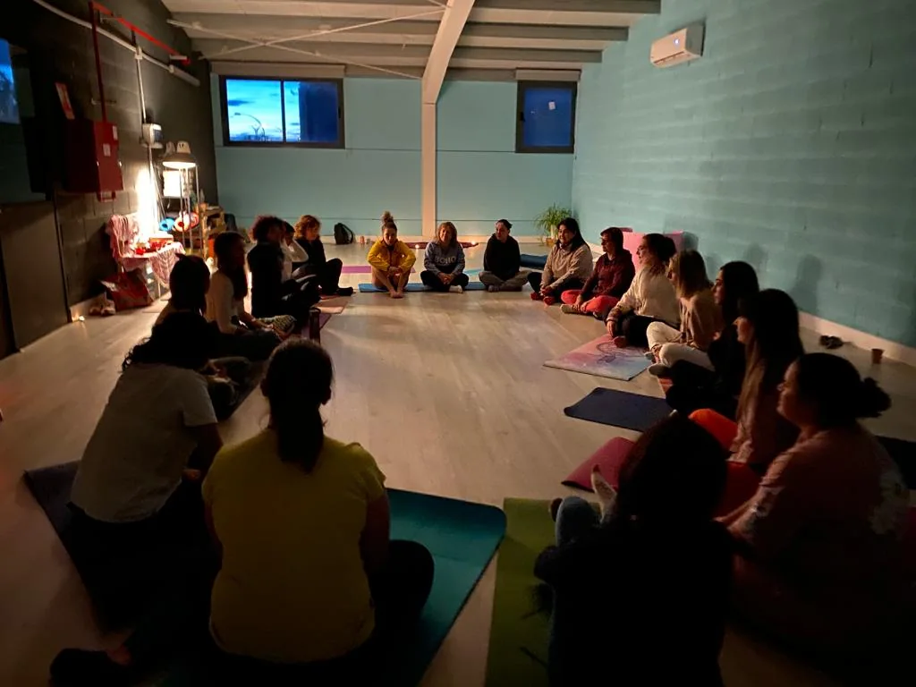 Participantes sentadas en círculo en el suelo de una sala con luz tenue