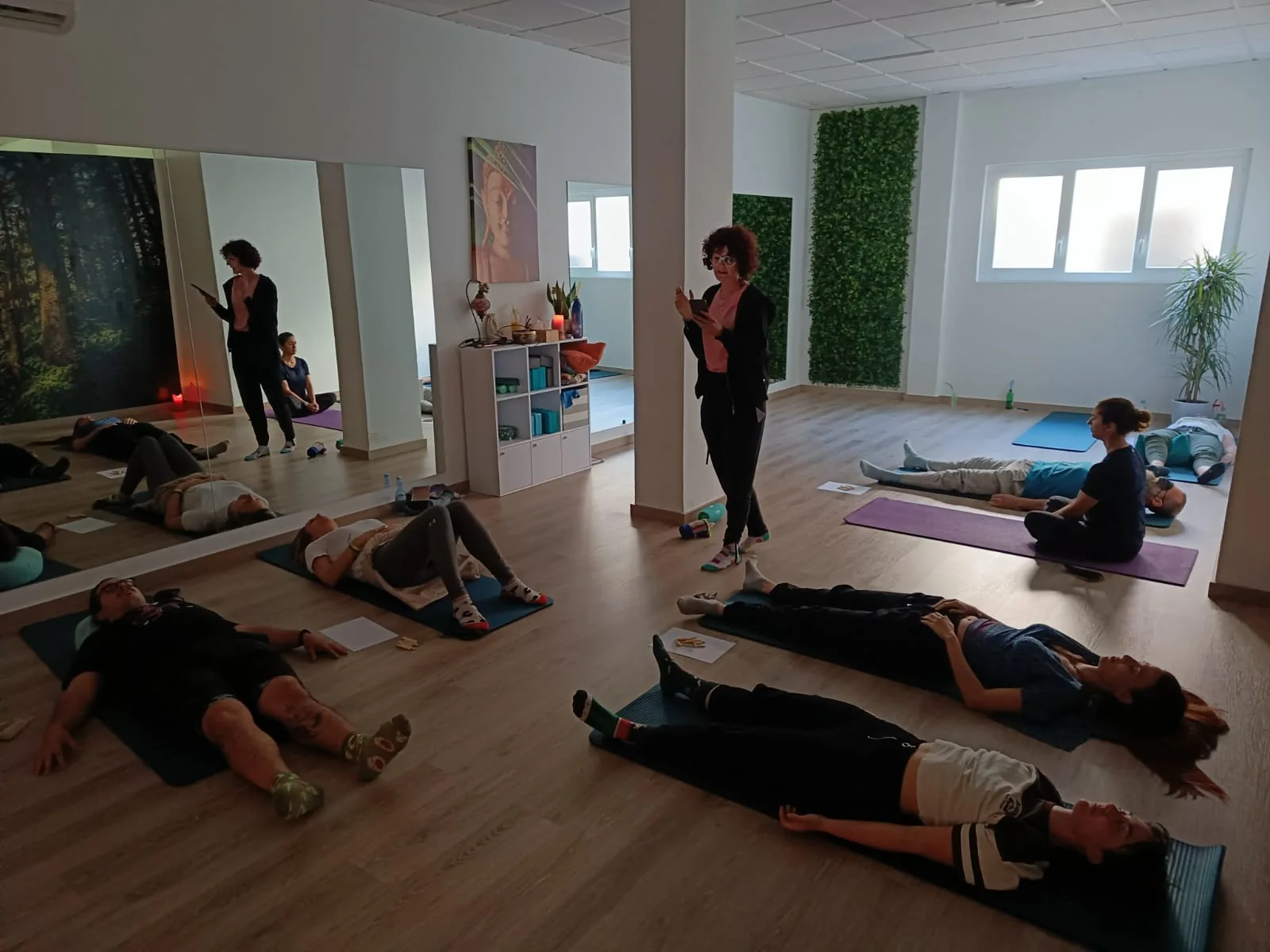 Participantes tumbadas en esterillas en una sala de taller, mientras una persona de pie guía la sesión